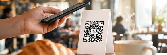 Hand holding a smartphone to scan a QR code on a cafe table card