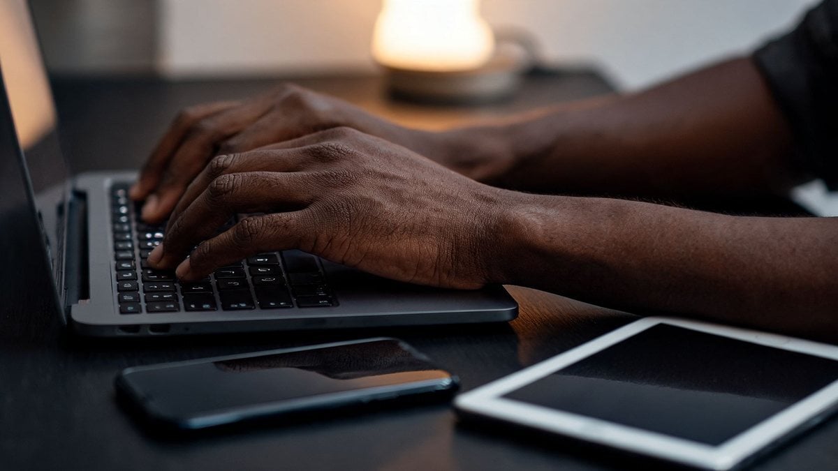 Hands typing on a laptop with a smartphone and tablet on the desk beside it
