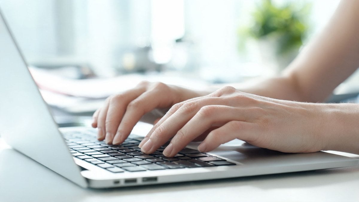 Hands typing on a laptop keyboard in a bright office